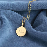 Image shows the back of the Organic Circle Blue Moon Necklace engraved with believe