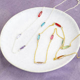 Image shows silver and gold Oval Mid Length Family Birthstone Station Necklace in a white trinket dish