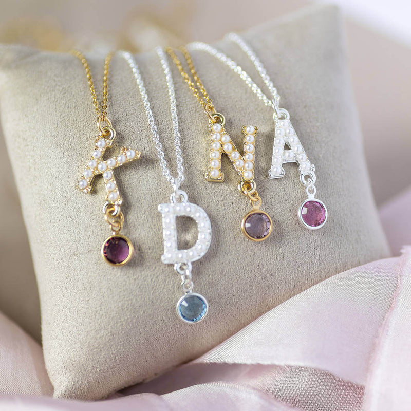 Two silver and  2 gold pearl alphabet initial birthstone necklace sitting a grey jewellery pillow.