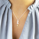 Model wears silver pearl alphabet necklace with gold star and the initial E