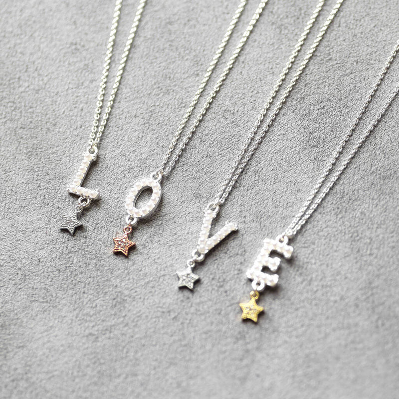 Four pearl alphabet necklaces with stars lying on grey background.All silver with the initials L O V E 2 with silver star, one with rose gold and one with gold 