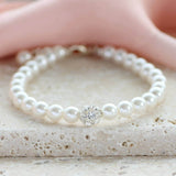 Pearl and crystal glitter ball bracelet lying on a stone board with pink material behind