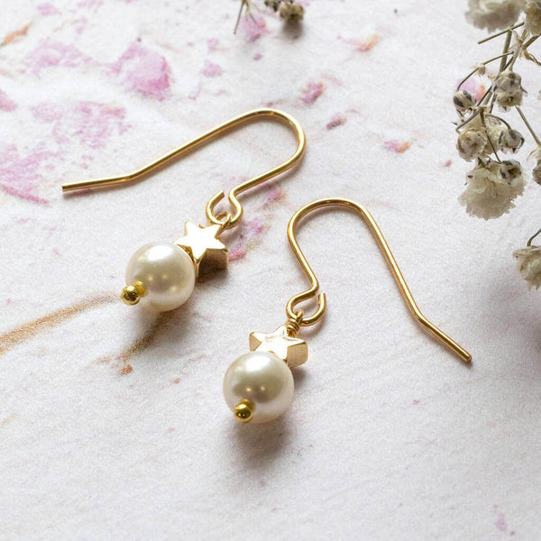 Pearl and gold plated star drop earring lying on pink background with dried white flowers