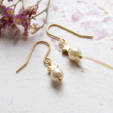 Pearl and gold plated star drop earring lying on pink background with dried dark pink and yellow flowers