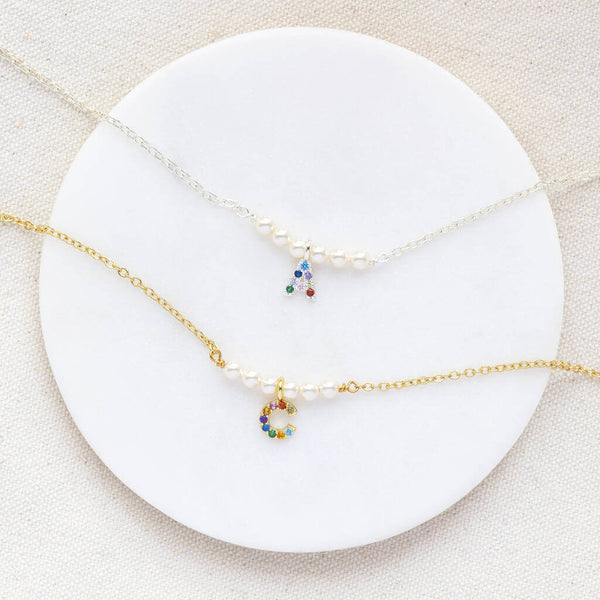 Gold and silver pearl bar necklace with rainbow initial gold has C and Silver has A lying-in a white circle board