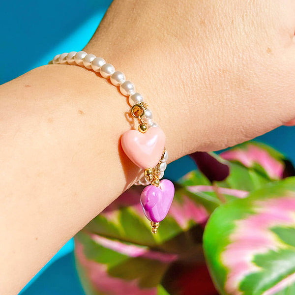 Image shows model wearings a pearl bracelet with pink and purple hearts