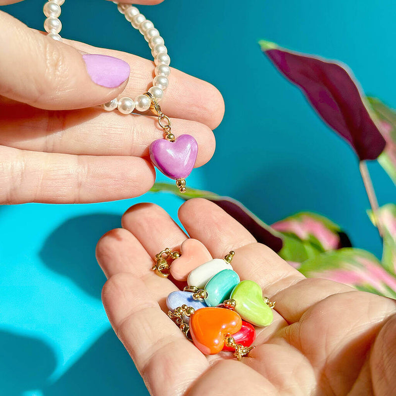 Image shows models hands holding pearl bracelet with multi-coloured heart charms