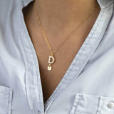 Model wears pearl studded initial and  heart charm necklace with the pearl initial and charm with heart 