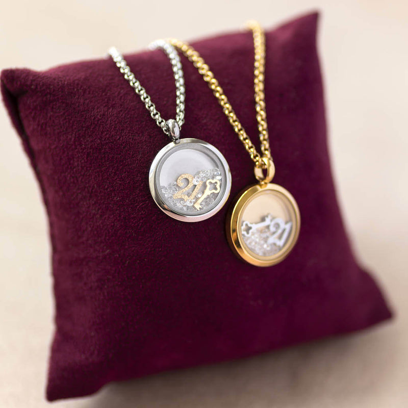 Images shows gold and silver personalised 21st birthday floating locket  on a maroon jewellery pillow