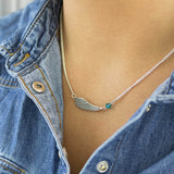 Image shows model wearing personalised angel wing necklace with December birthstone