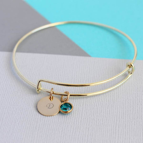 Image shows gold personalised bangle with gold  disc engraved with the initial d and blue zircon birthstone