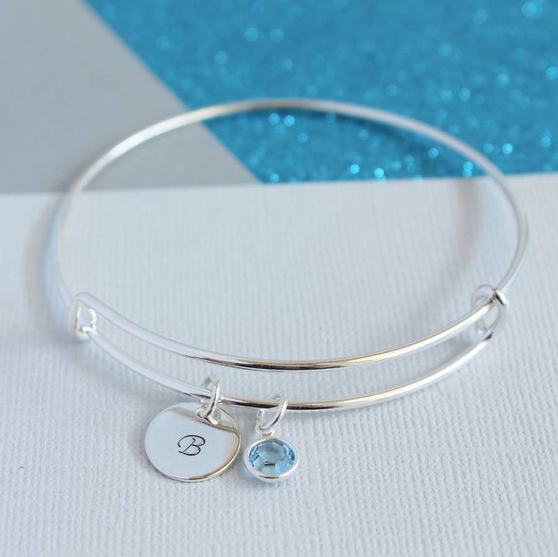 Image shows silver personalised bangle with silver disc engraved with the initial B and aquamarine birthstone