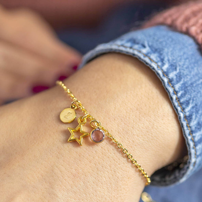 Image shows model wearing personalised gold star birthstone charm bracelet with E initial on disc and June birthstone