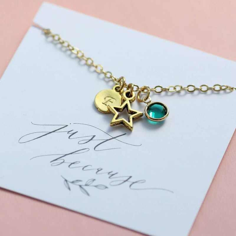 Image shows personalised gold star birthstone charm bracelet with E initial on disc and September birthstone on a just because sentiment card