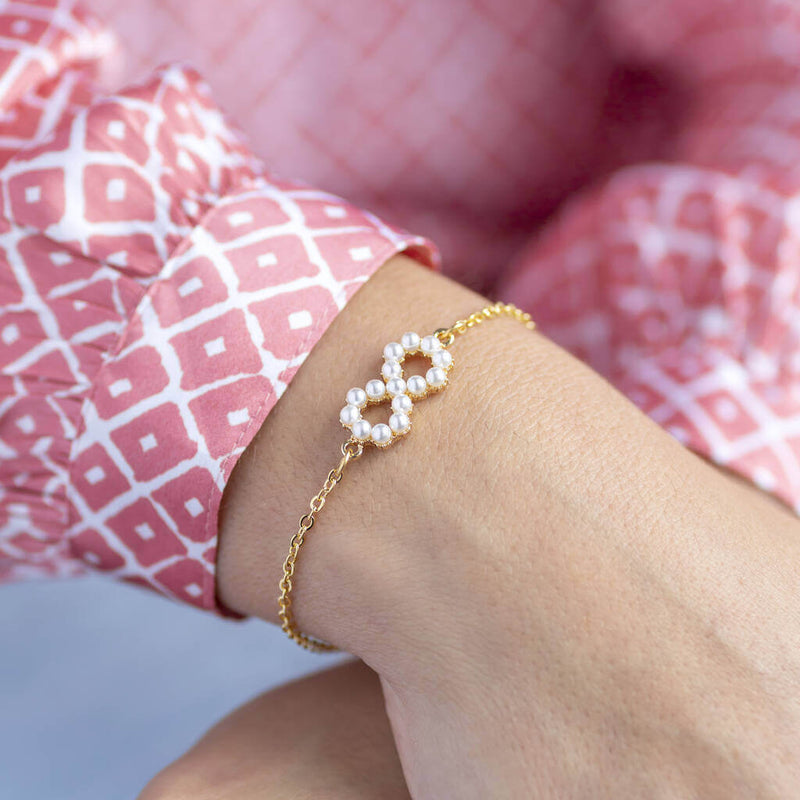 Model wears gold plated personalised infinity bracelet with pearl detail 