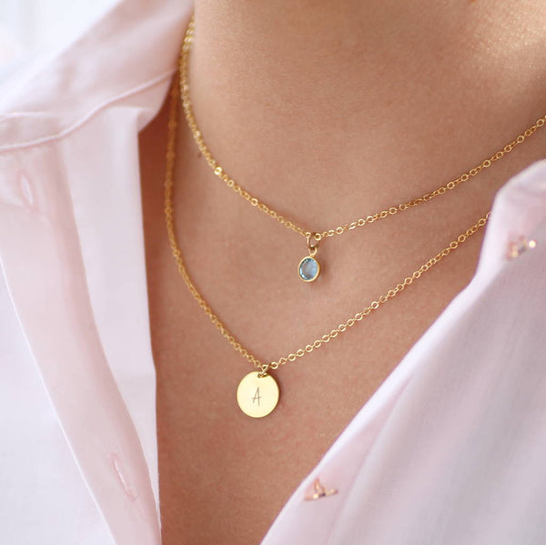 Image shows model wearing personalised layered birthstone necklace with March birthstone and Initial disc with A on it