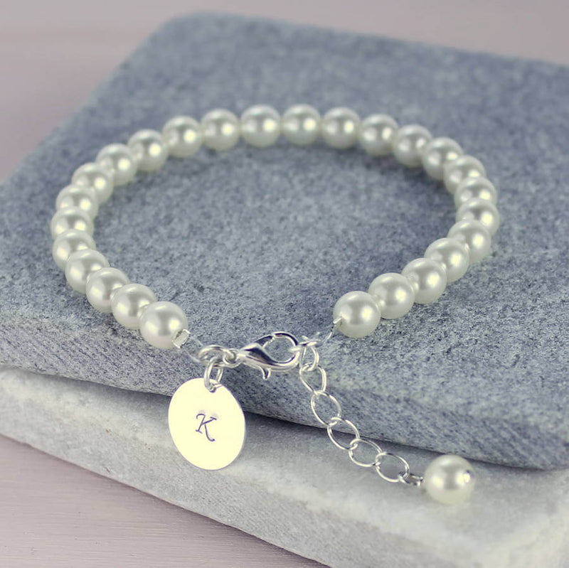 Personalised pearl disc bracelet lying on a grey tile with the disc initial K hanging off