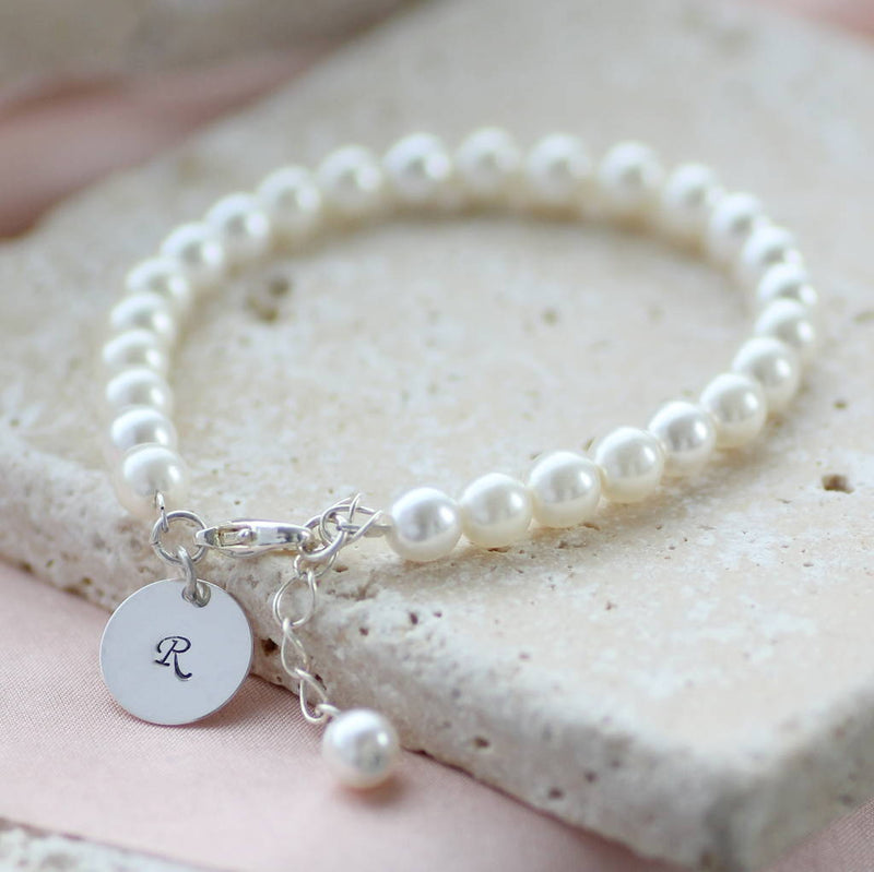 Personalised pearl disc bracelet lying on a cream tile with the disc initial R hanging off