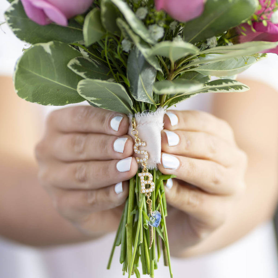 Bride holds bouquet with personalised something blue bride and groom charm attached in gold with pearl initial S and B