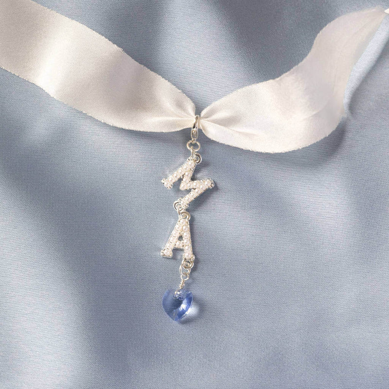 The personalised something blue bride and groom charm in silver attached to a piece of chiffon lying on blue material with pearl initial M and A