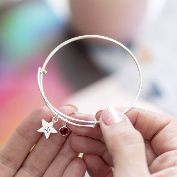 Image shows model holding  personalised star birthstone bangle with initial M on the star and July birthstone