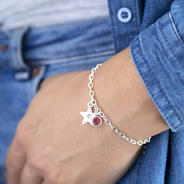 Image shows model wearing personalised star charm bracelet with a star engraved with the letter R and October birthstone