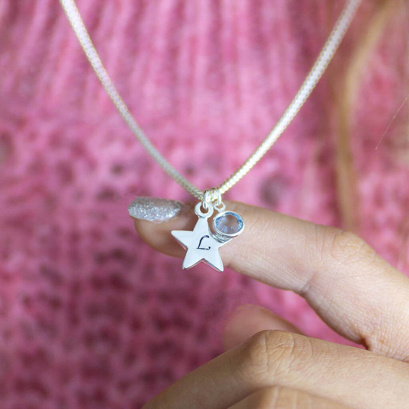 Image shows model holding personalised star charm necklace with L on the star and March birthstone