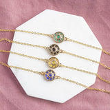 Image shows blue, yellow,black and green Personalised Sun Symbol Bracelets on a white  hexagon coaster