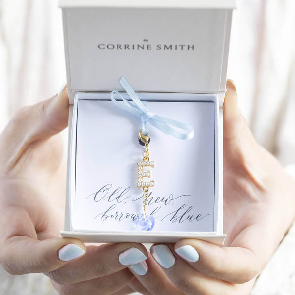 Model holds a box with the personalised pearl initial something blue charm in gold with the initial E attached to it is a blue crystal heart charm on the old new borrowed blue sentiment card