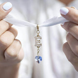 Model hold a piece of white chiffon with the personalised pearl initial something blue charm in silver  with the initial E attached 