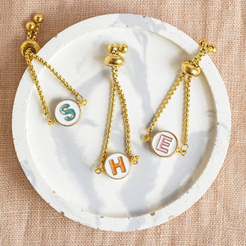 Image shows a selection of Image shows model wearing Round Enamel Initial Chain Slider Ring with the initials S, H and E