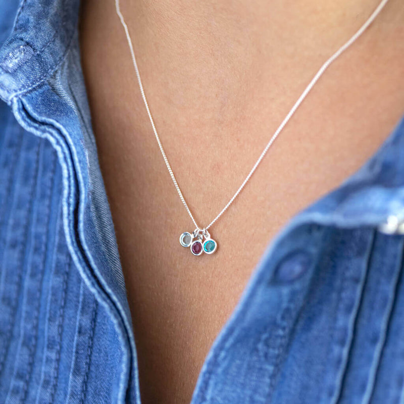 Image shows model wearing silver mini family birthstone charm necklace with April, February and  December birthstones
