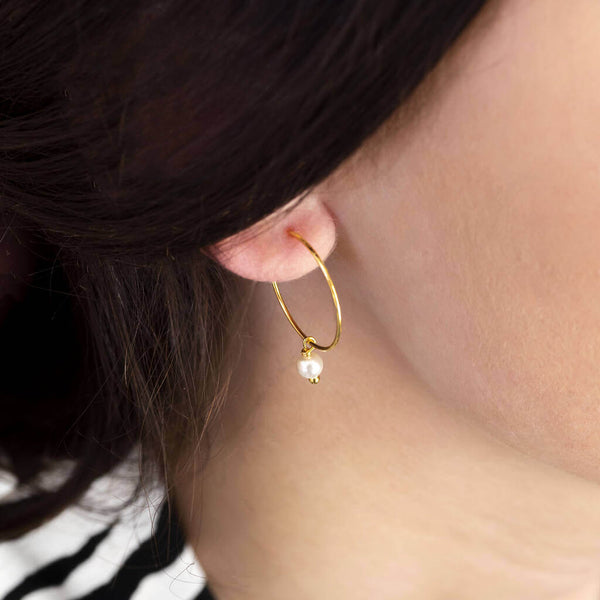 Image shows model wearing  simple gold pearl hoop earrings