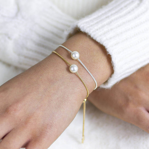 Model wears gold plated single floating pearl sliding bracelet and silver plated single floating pearl sliding bracelet.