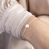 Model wears silver plated single floating pearl sliding bracelet. 