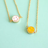 Image shows yellow and white Smiley Face Necklaces on a green background