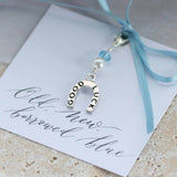 Something blue lucky horseshoe charm attached to old new borrowed blue sentiment card with baby blue ribbon lying on stone surface