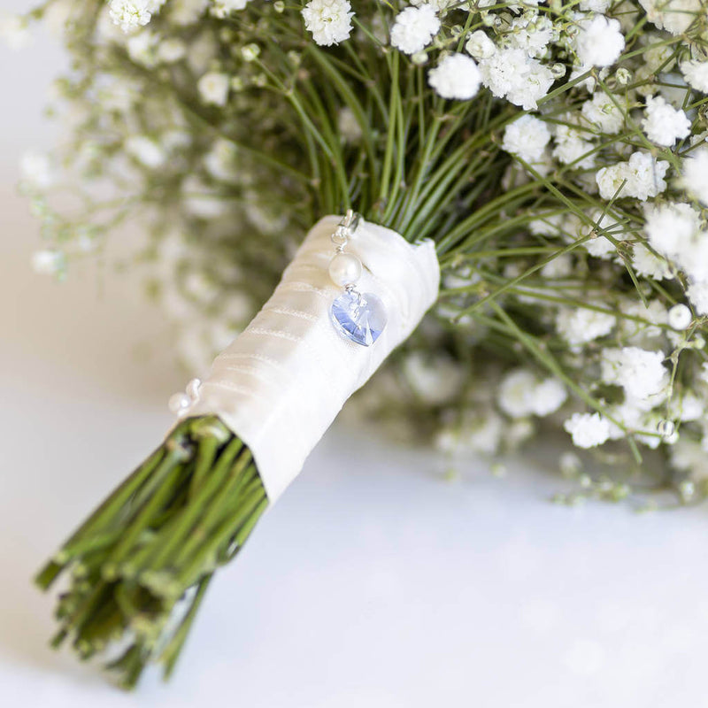 Image shows something blue Swarovski crystal bridal charm on a white bridal bouquet attached with ivory ribbon.