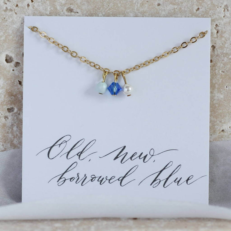 Image shows gold plated something blue chain anklet with three charms from left to right - pale blue pearl, Swarovski crystal bead and ivory dainty pearl. Anklet is mounted on an 'old, new, borrowed, blue' sentiment card,