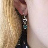 Image shows model wearing sterling silver heart birthstone earrings with May birthstone