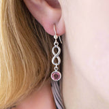 Image shows model wearing sterling silver infinity birthstone earrings with October birthstone