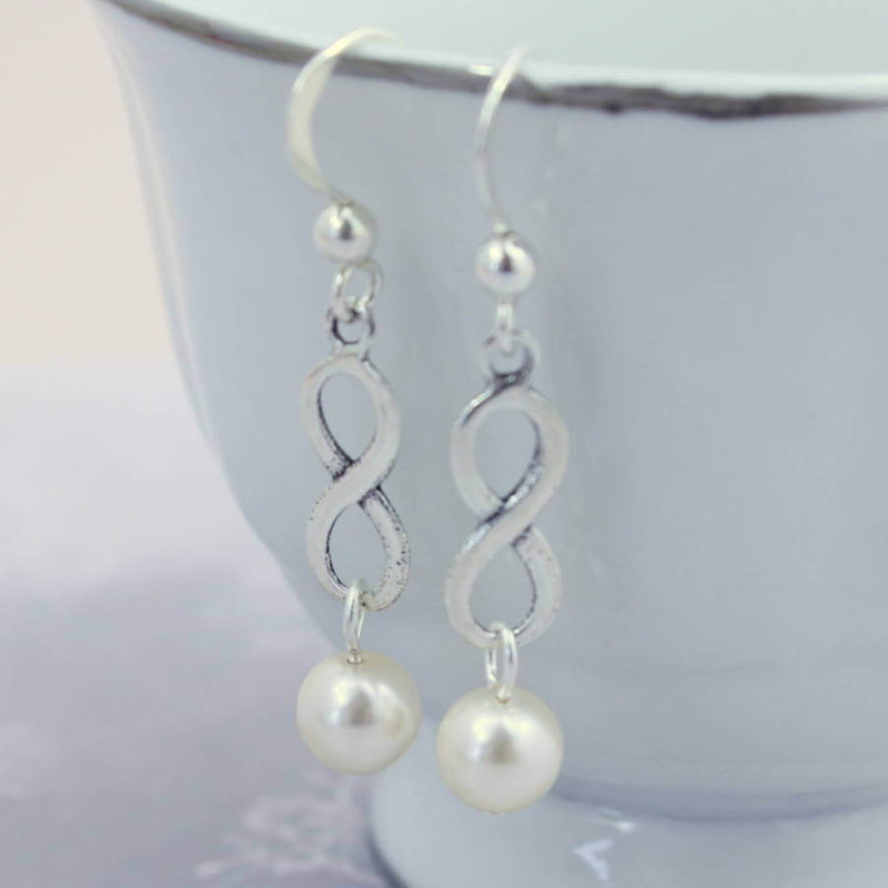 Image shows Sterling Silver Infinity Pearl Earrings hanging from a white bowl