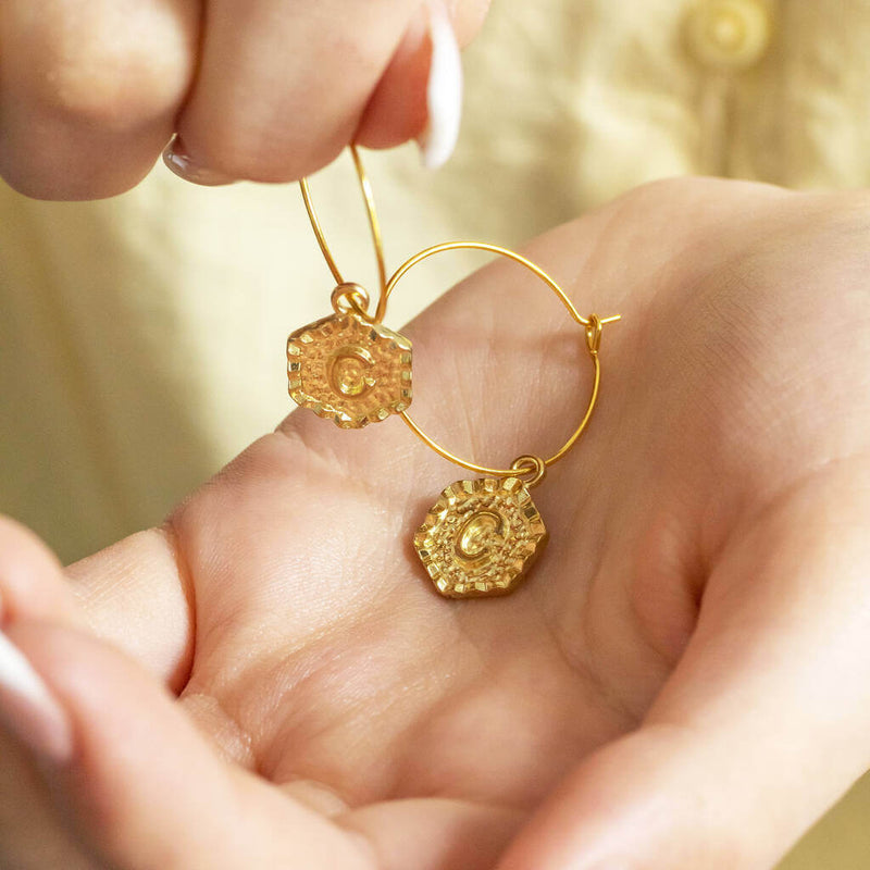 Image shows model holding gold Textured Hexagon Initial Hoop Earrings