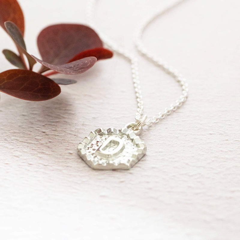 Images shows silver textured hexagon initial necklace with the initial D