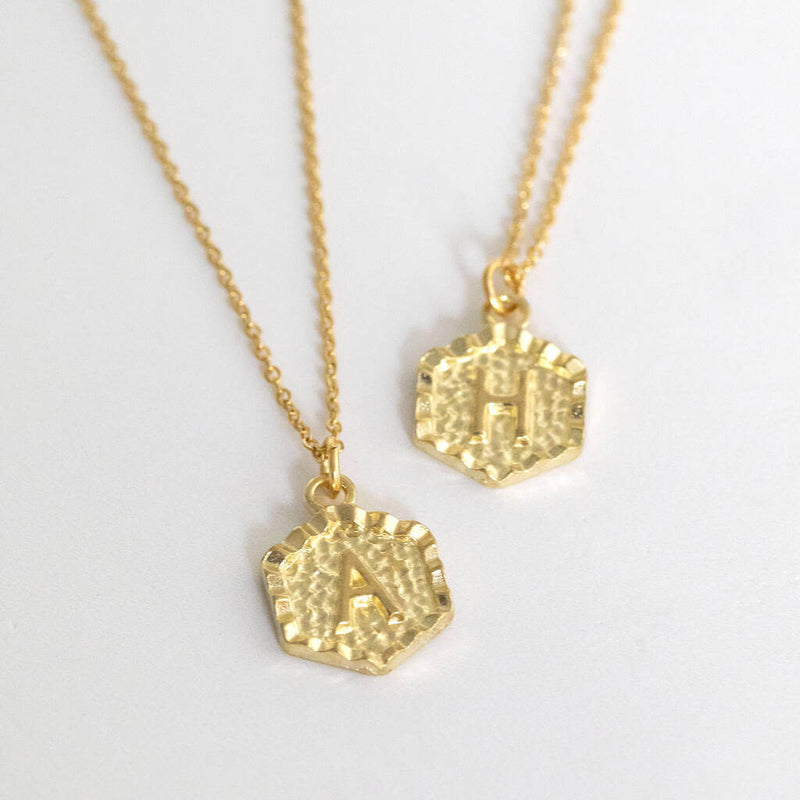 Image shows two gold textured hexagon initial necklace with initial A & H