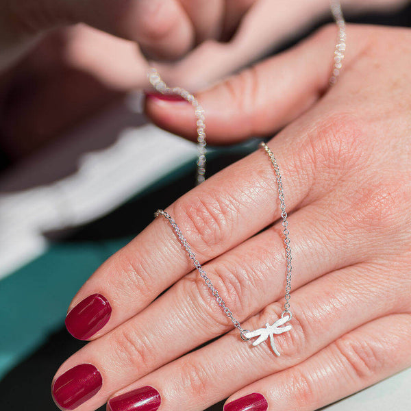 Image shows model holding tiny dragonfly symbolic necklace