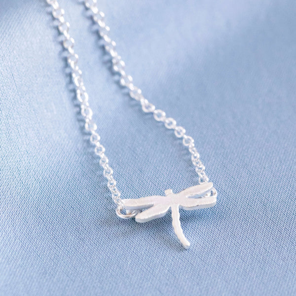 Image shows Tiny Dragonfly Symbolic Necklace on a blue background