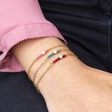 Image shows model wearing three tiny gold crown birthstone bar bracelets, October,December and July birthstones