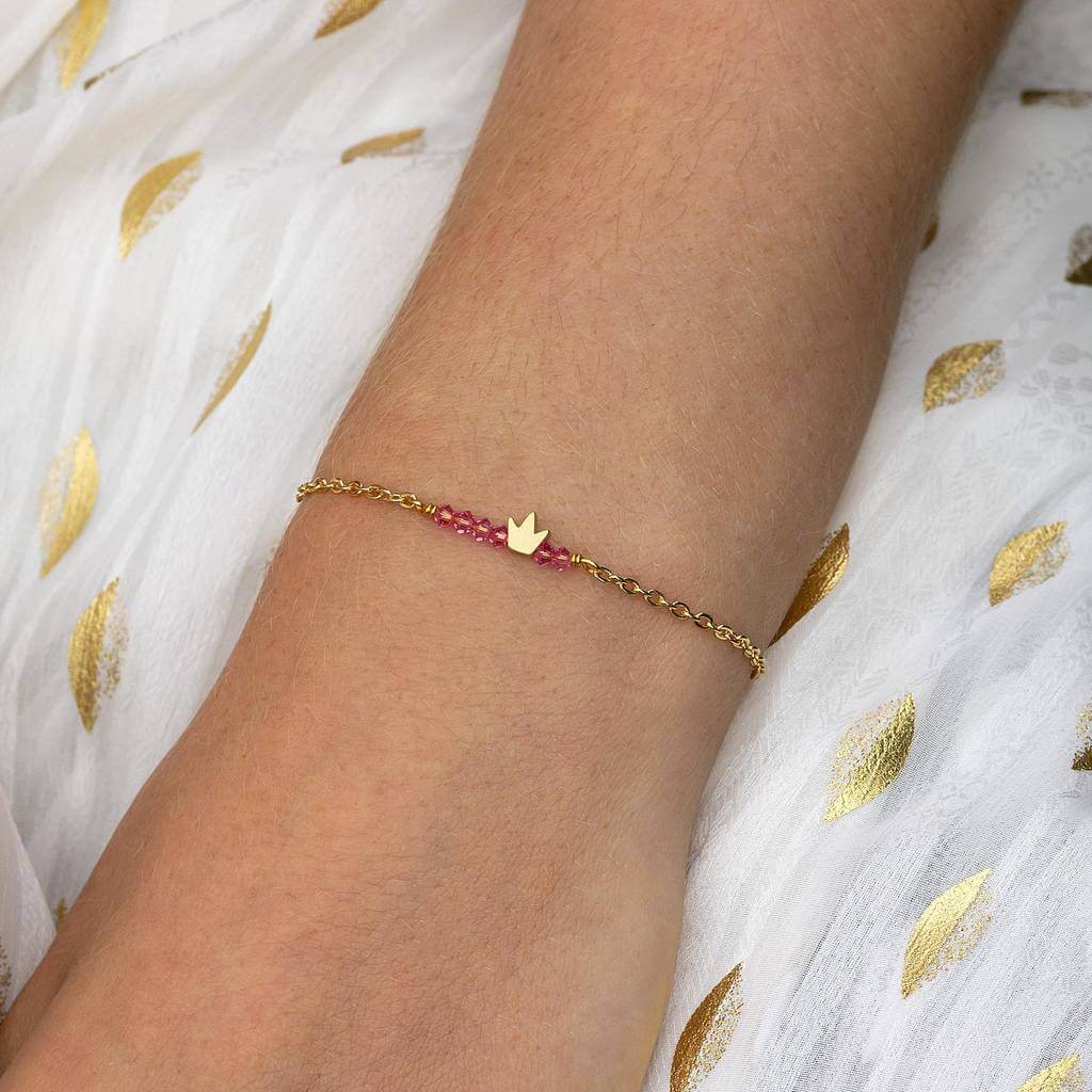 Image shows model wearing tiny gold crown birthstone bar bracelet with October birthstone