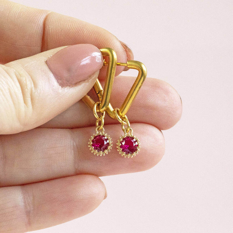 Image shows model holding Triangle Huggie Earrings with Birthstone Detail